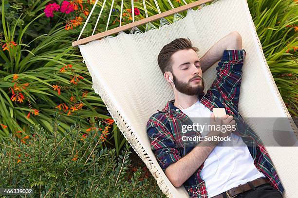 young man relaxing on hammock listening to music - young man listening music and relaxing in hammock stock pictures, royalty-free photos & images