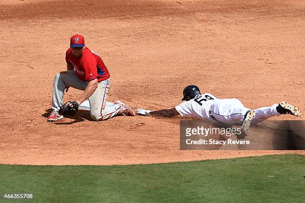Xavier Avery of the Detroit Tigers beats a tag by Cord Phelps of the Philadelphia Phillies during a spring training game at Joker Marchant Stadium on...