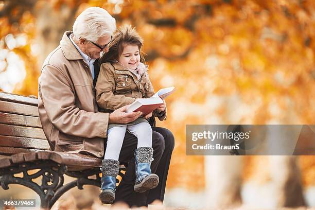 grandfather reading a book to little girl in the park. - reading old young stock pictures, royalty-free photos & images