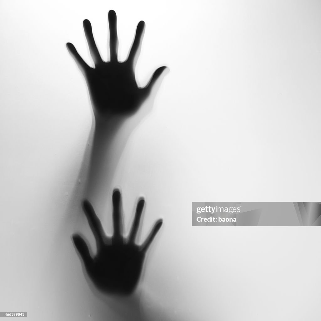 Two hands in silhouette pressed against frosted glass