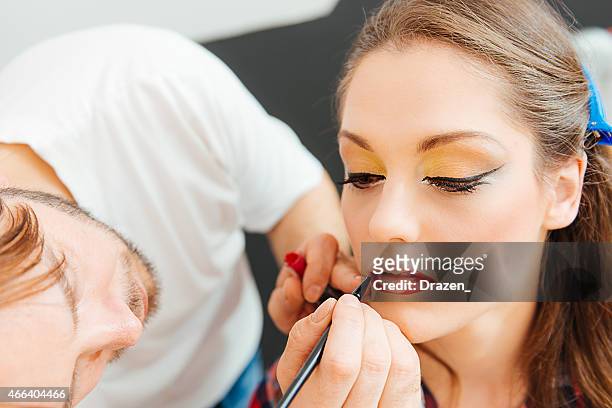 make up artist puts lipstick on beautiful female fashion model - lip liner stock pictures, royalty-free photos & images