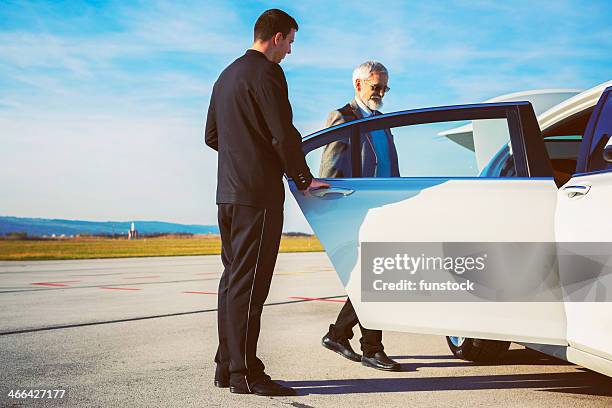 driver helping senior adult into limousine at airport - limousine stock pictures, royalty-free photos & images