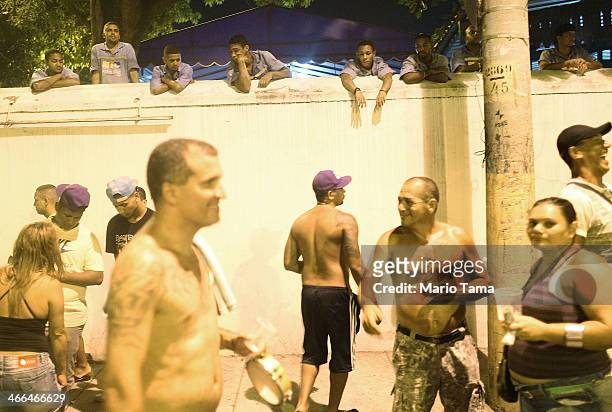 Revelers gather beneath Porto Maravilha workers looking on behind a fenced-in construction project in the first street parade of the 2014 Carnival...