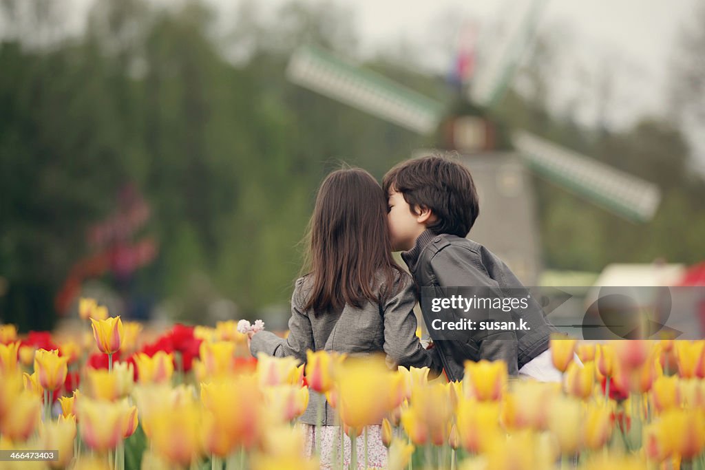 Boy kissing sister on cheek surrounded by tulips.