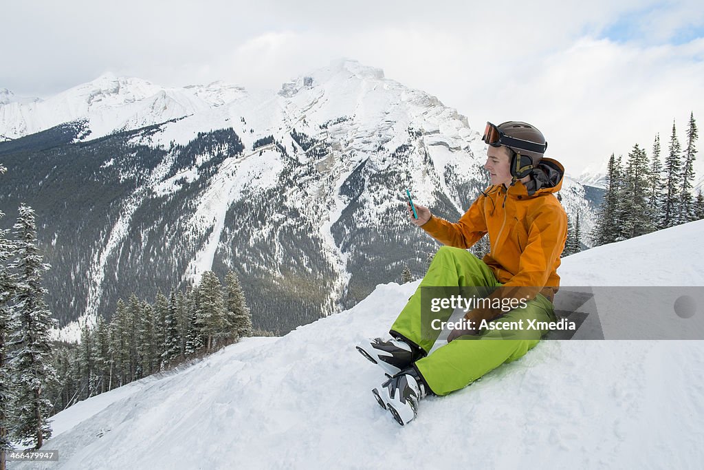 Skier pauses to text/take picture from snow edge