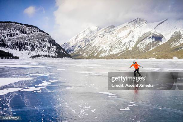 woman skates across frozen lake, in mountains - provinz alberta stock-fotos und bilder