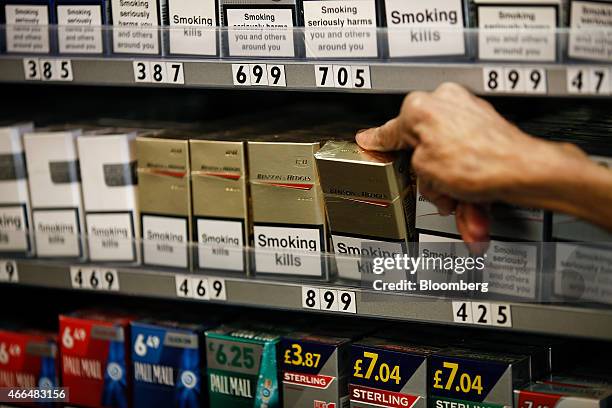 "Smoking Kills" and other warning labels sit on boxes of cigarettes as a shopkeeper reaches for a packet of Benson and Hedges cigarettes, produced by...