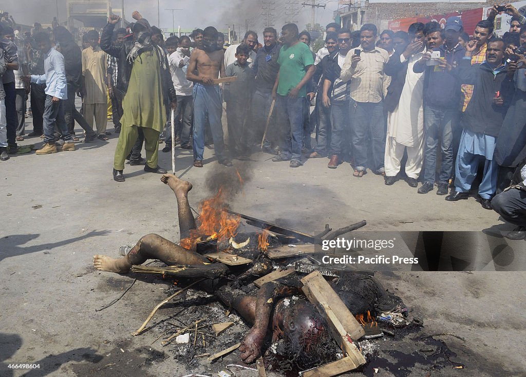 People gather around the burning bodies of what the mob...