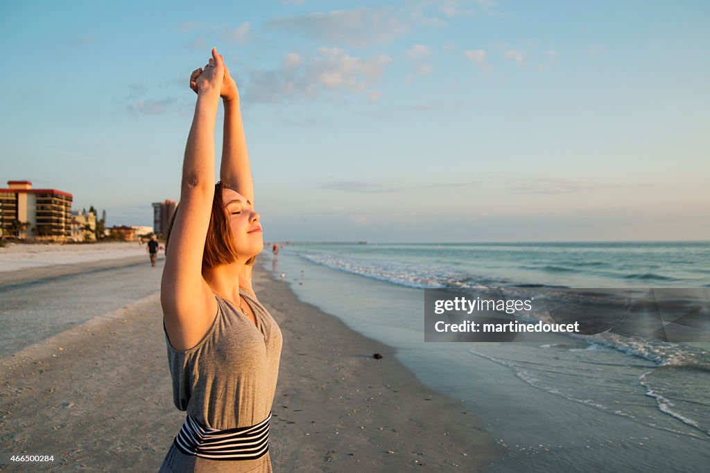 Mujer joven de estiramiento y disfrutar de la puesta del sol en la playa.