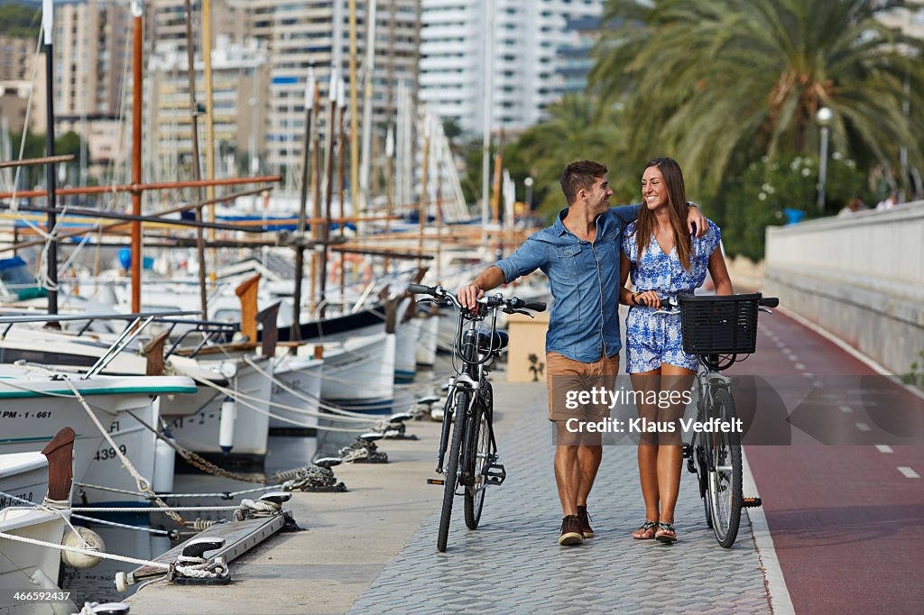 Couple walking with bikes at small harbor