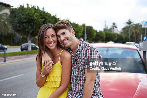 couple hugging while leaning against red car - leaning stock pictures, royalty-free photos & images