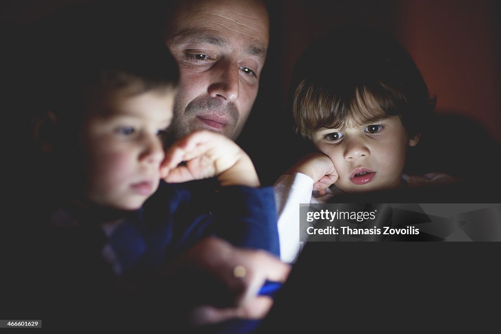 Father with his kids using a tablet in the dark
