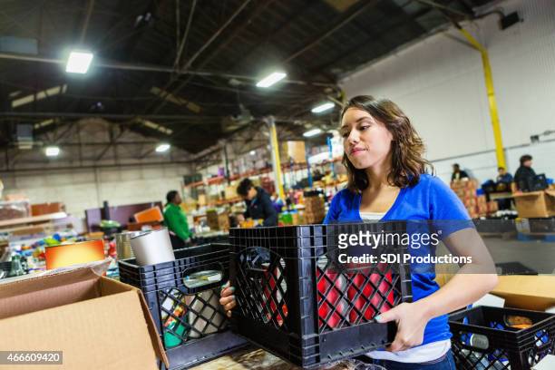 giovane donna fare volontariato per organizzare le donazioni di cibo in grande banca - cassetta degli attrezzi foto e immagini stock