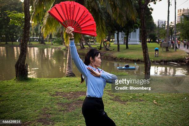 Woman holding a red fan practices tai chi at Lumphini Park in Bangkok, Thailand, on Sunday, March 15, 2015. Almost a third of Thailand's population...