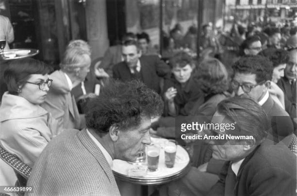 Swiss artist Alberto Giacometti talks with another man at a crowded cafe, Paris, France, May 12, 1954.