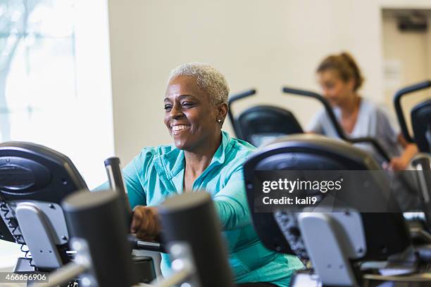 senior donna afro-americana in palestra su cyclette - black woman riding bike foto e immagini stock