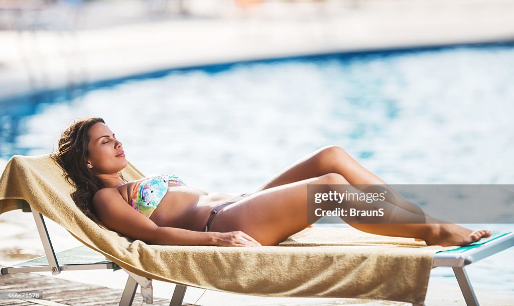 Woman sunbathing on deck chair near the swimming pool.