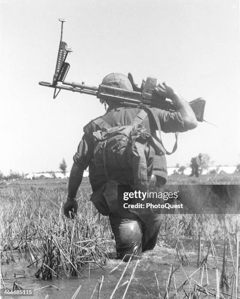 Marines crossing a rice paddy while on patrol, holding an M-60 machine gun, Vietnam, 1966.