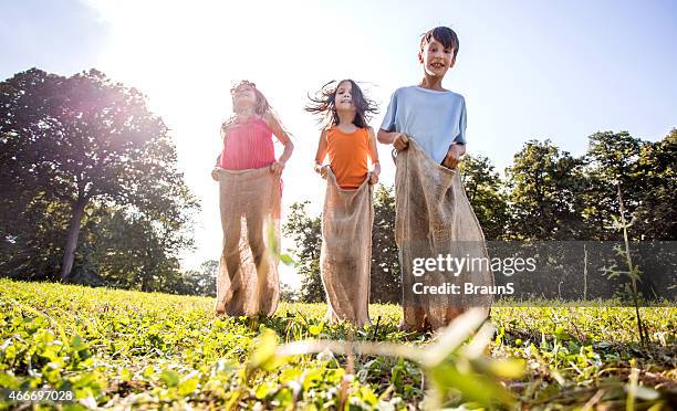 below view of three happy kids on sack race outdoors. - sack race stock pictures, royalty-free photos & images