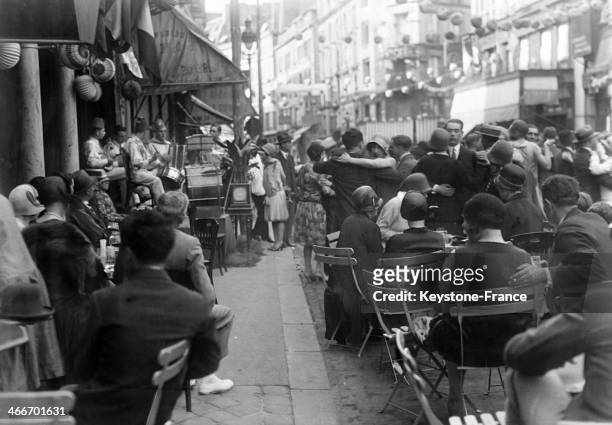 People having drinks on a cafe terrace looking at dancers in the street on Bastille Day, on July 14, 1929 in Paris, France.