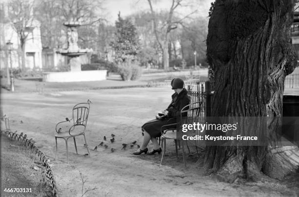 Woman seated in a park with birds around her in December 1928 in Paris, France.