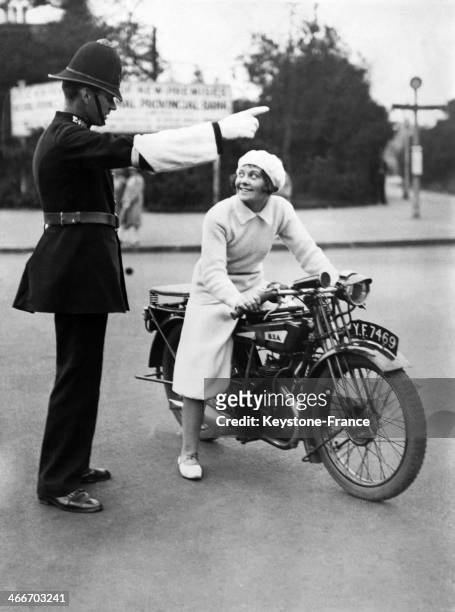 Circa 1920: Miss 1928 on motorcycle wearing divided skirt, asking for her way to a policeman circa 1920 in London, United Kingdom.