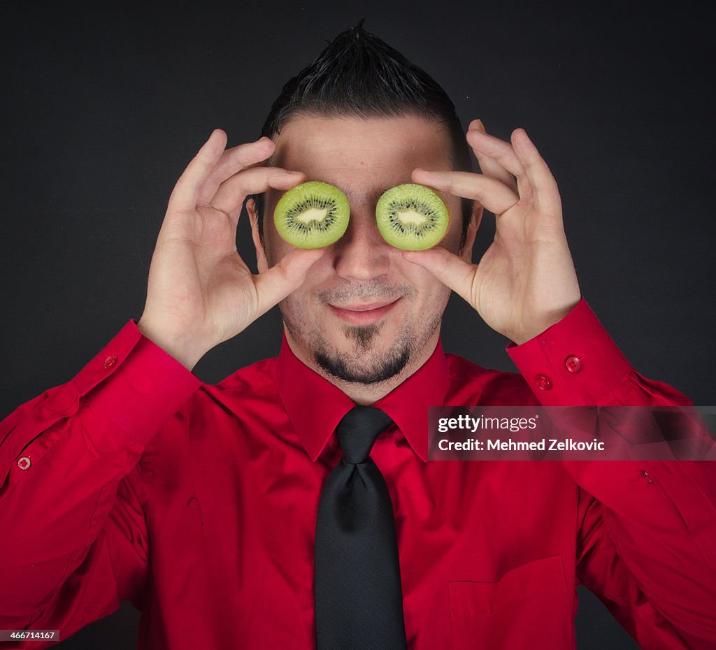 Young man holding kiwi over his eyes