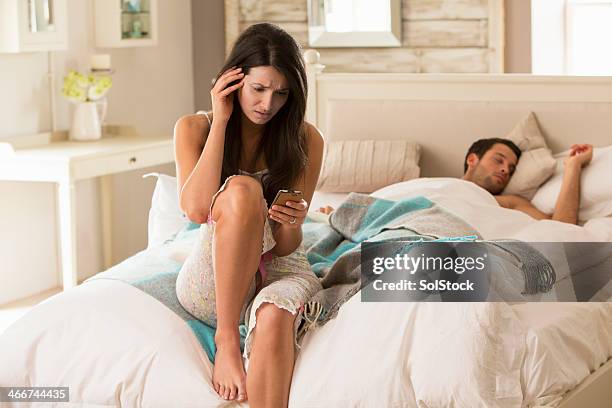 distraught woman holding mobile phone in bed - suspicion infidelity stock pictures, royalty-free photos & images