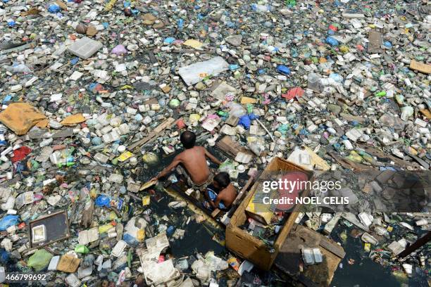 Father and son on a makeshift boat made from styrofoam paddle through a garbage filled river as they collect plastic bottles that they can sell in...