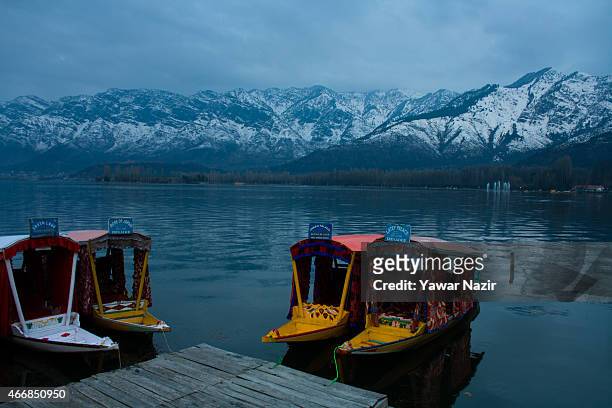 Shikara boats are moored to the bank of Dal lake as the snow capped Zabarvan mountains are reflected on March 19, 2015 in Srinagar, the summer...
