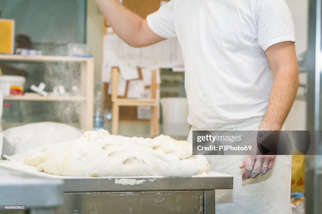 Baker putting flour on leavened dough on working table