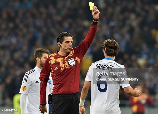 German referee Deniz Aytekin shows a yellow card to Dynamo Kiev's Aleksandar Dragovic during the UEFA Europa League round of 16 football match...