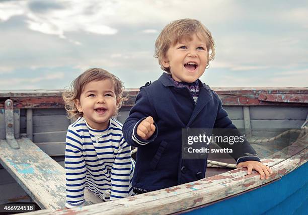 two smiling children playing in a worn rowboat - kids fashion stockfoto's en -beelden