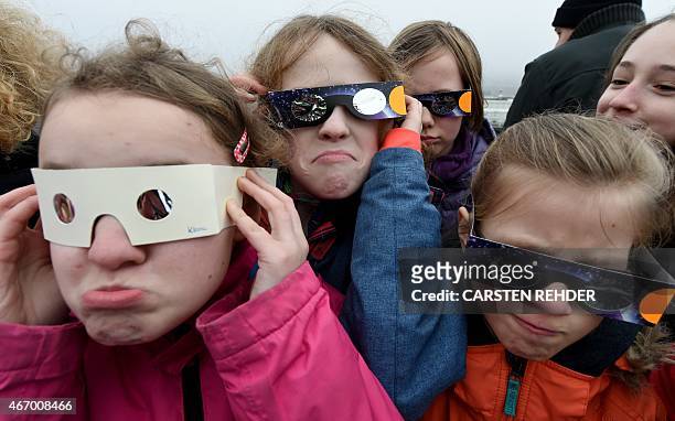 Girsl use protective glasses to catch a glimpse of a solar eclipse as they stand in front of the observatory's cupola on the roof of the university...