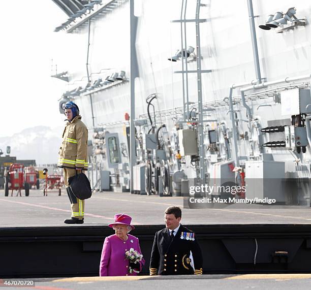 Queen Elizabeth II accompanied by Captain Timothy Henry uses an aircraft lift to reach the flight deck of HMS Ocean before departing by helicopter,...