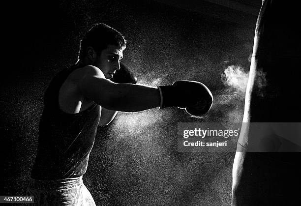 greyscale image of a boxer having a go at the punching bag - bokshandschoen stockfoto's en -beelden