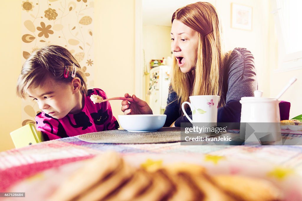 Mother feeding fussy daughter breakfast