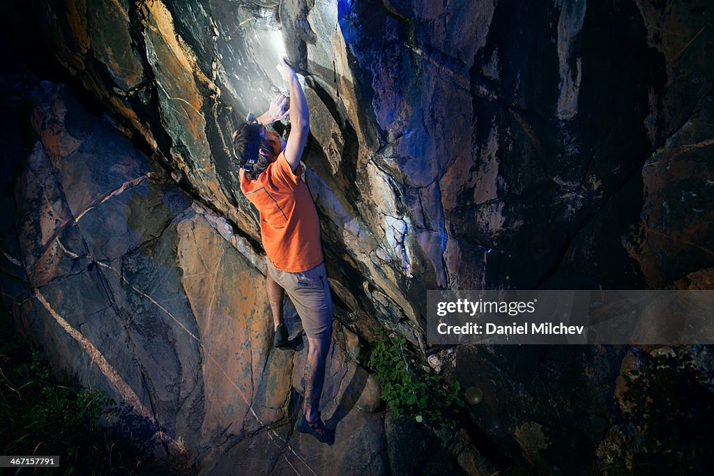 Men bouldering at night with a headlamp on.