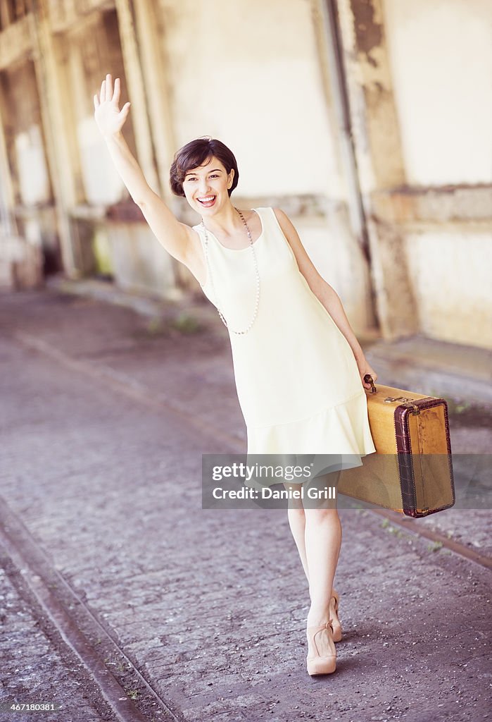USA, New Jersey, Jersey City, Woman in dress holding suitcase at train station, waving hand