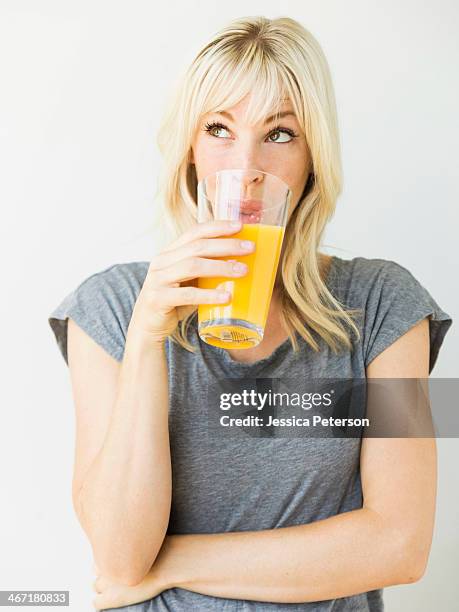 studio portrait of blonde woman drinking orange juice - fruit juice stock pictures, royalty-free photos & images