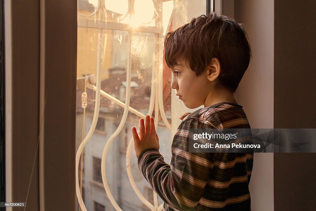 Profile of sad boy looking through the window