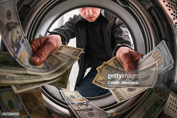 caucasian male criminal throwing money inside a laundry machine - money laundering stock pictures, royalty-free photos & images