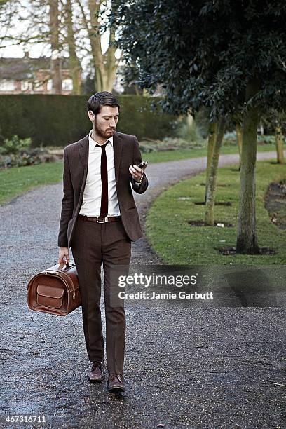 gentleman looking at his phone walking - bruin pak stockfoto's en -beelden