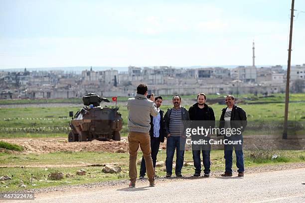 Kurdish men have their photo taken with the ruined Syrian town of Kobani in the background on March 22, 2015 in Suruc, in the province of Sanliurfa,...