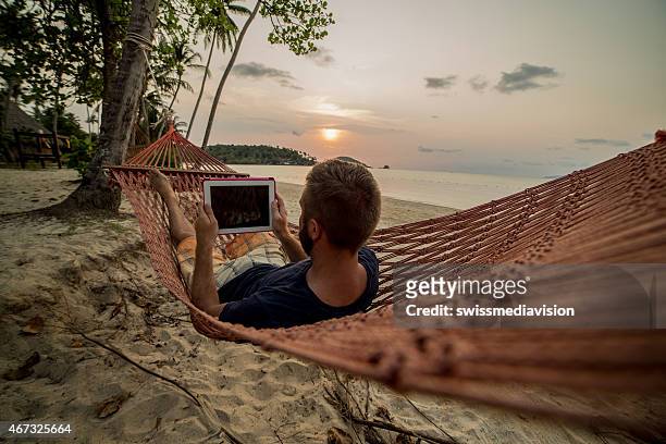 man on hammock relaxing-digital tablet - beach hammock stock pictures, royalty-free photos & images