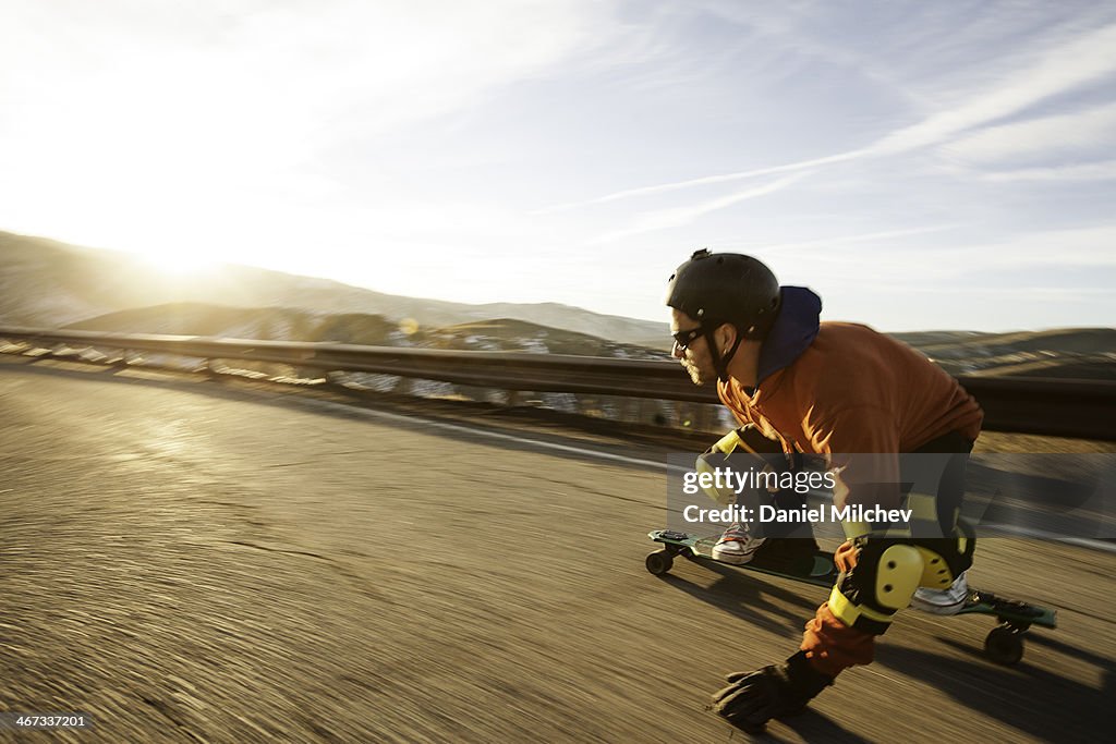 Lonboard skateboarder going down a road at sunset.
