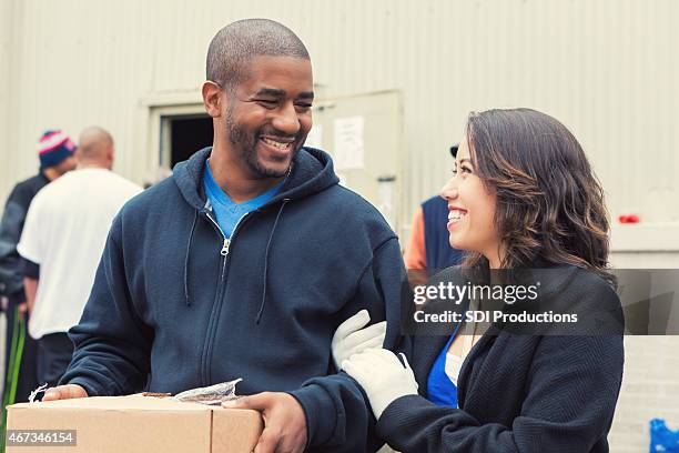 volunteer carrying box of groceries for woman at food bank - homelessness help stock pictures, royalty-free photos & images