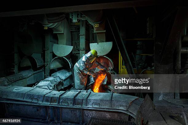 Worker wearing heat resistant clothing checks the flow of molten copper from a hot furnace at the KHGM Polska Miedz SA copper smelting plant in...