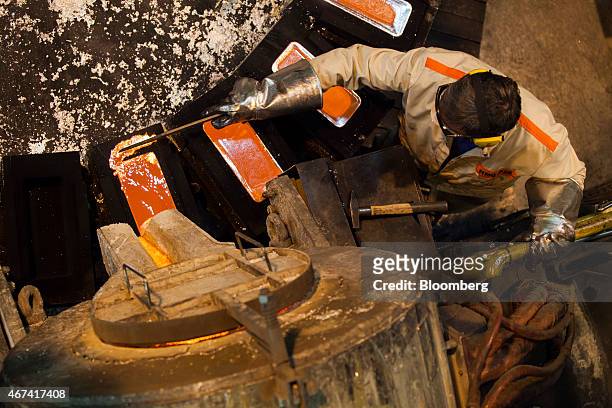 Worker uses a rod to clean up the edges of molten silver as it cools in a bullion bar mould at the KHGM Polska Miedz SA smelting plant in Glogow,...