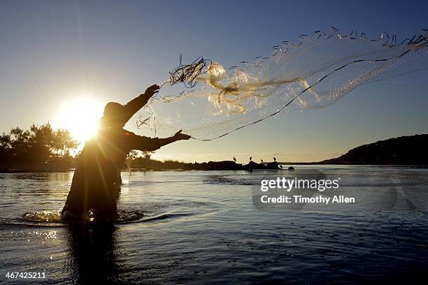 silhouetted laguna fisherman casts net at sunset - fishing net stockfoto's en -beelden